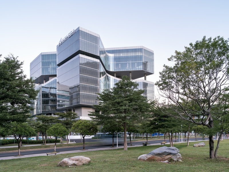 Cantilevered volumes rising above tree-lined plaza under overcast sky