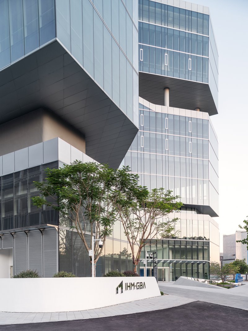 Street view of the stacked glass volumes with cantilevered dark slabs and a mature tree at the entrance