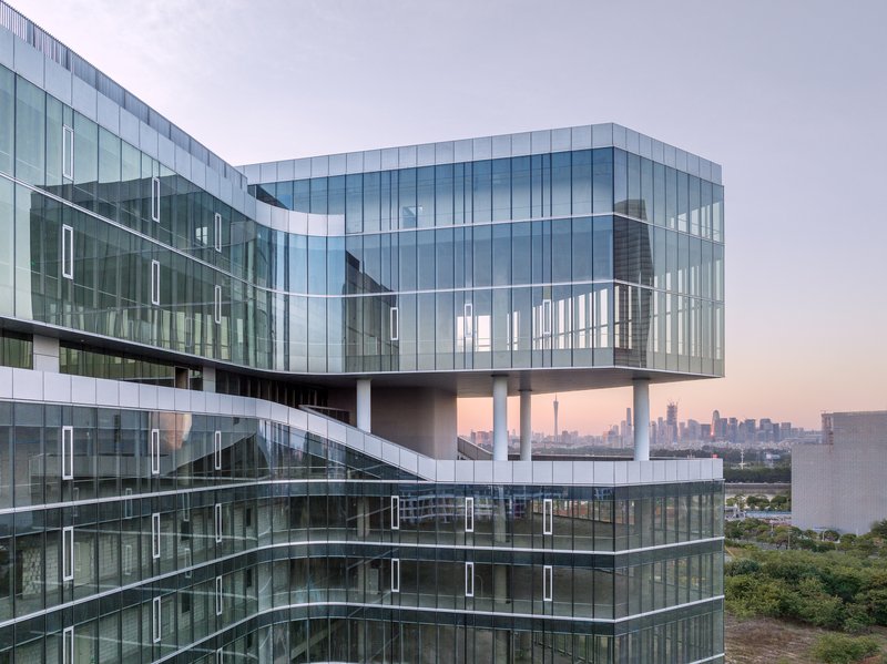 Corner facade showing the cantilevered glass volume raised on white columns at dusk