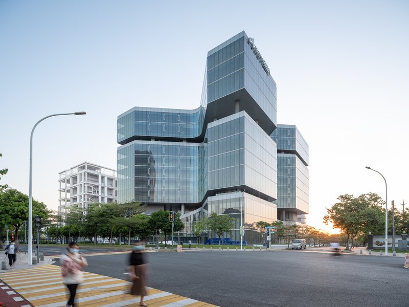 Stacked glass volumes wrapped with dark horizontal bands at an urban intersection at dusk