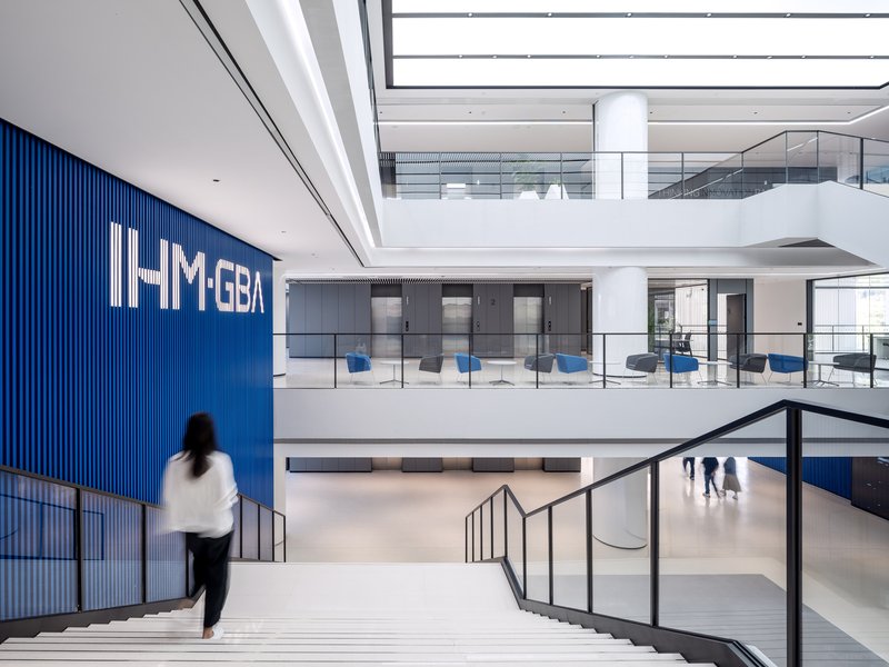 Multi-story atrium with white stairs descending past a blue corrugated wall and a person walking