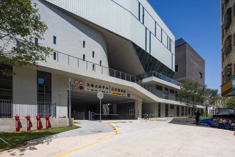 Covered entrance driveway with exposed concrete ceiling flanked by white metal cladding under clear blue sky