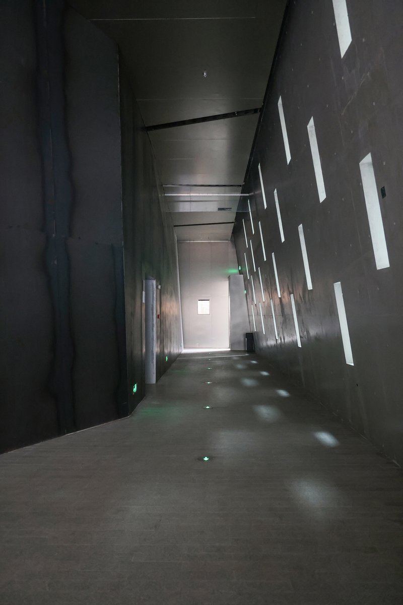 Dark corridor with vertical light slots piercing the concrete wall casting geometric shadows on the floor