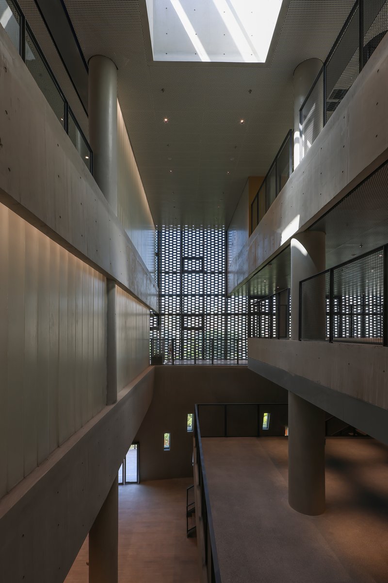 Double-height atrium with board-formed concrete walls, perforated screen and diagonal skylight above cylindrical columns