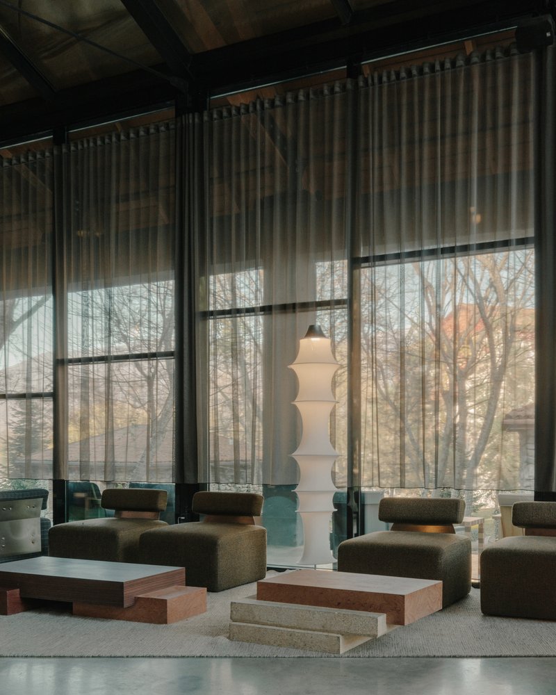 Lounge area with sheer curtains filtering daylight through steel-framed windows overlooking bare winter trees