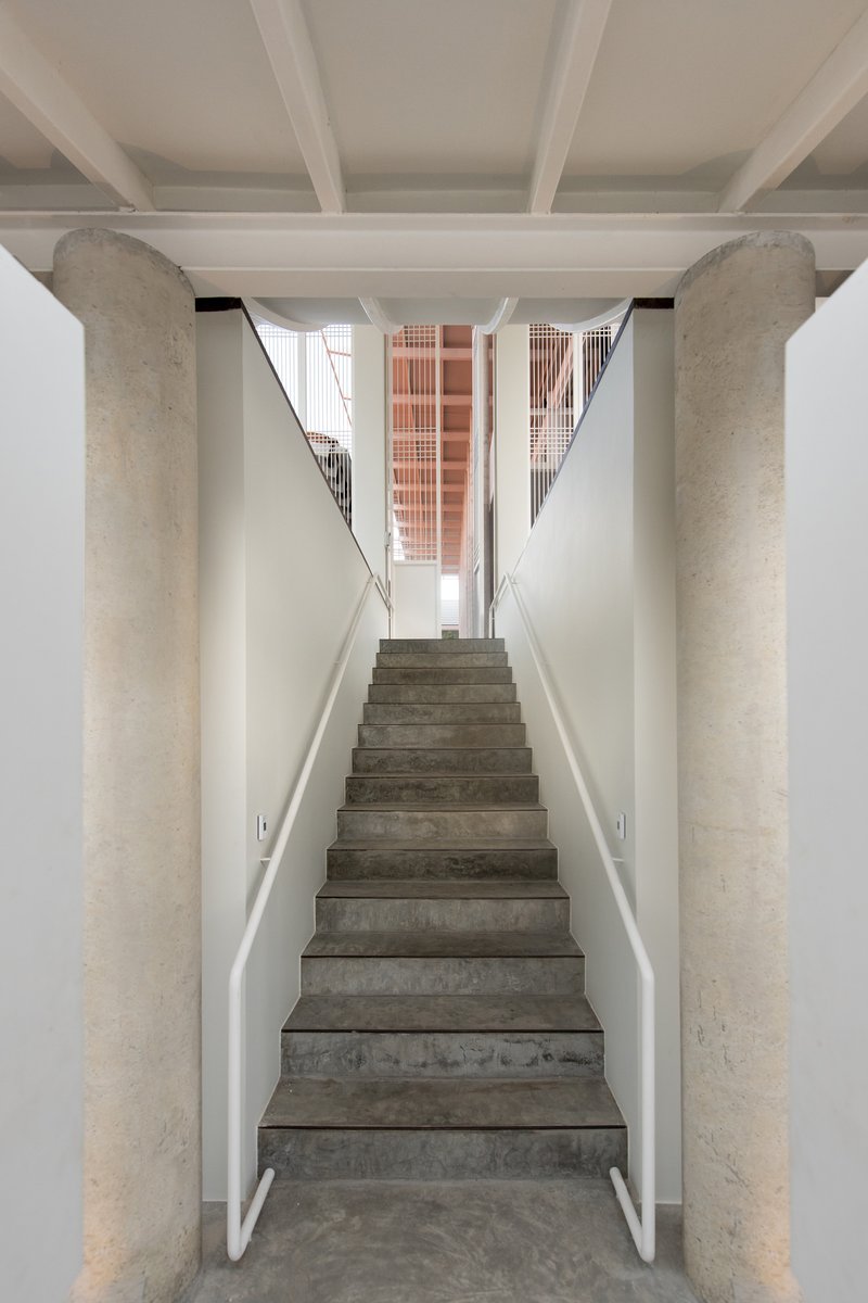 Concrete staircase flanked by cylindrical columns with exposed beams overhead and terracotta screen visible at landing