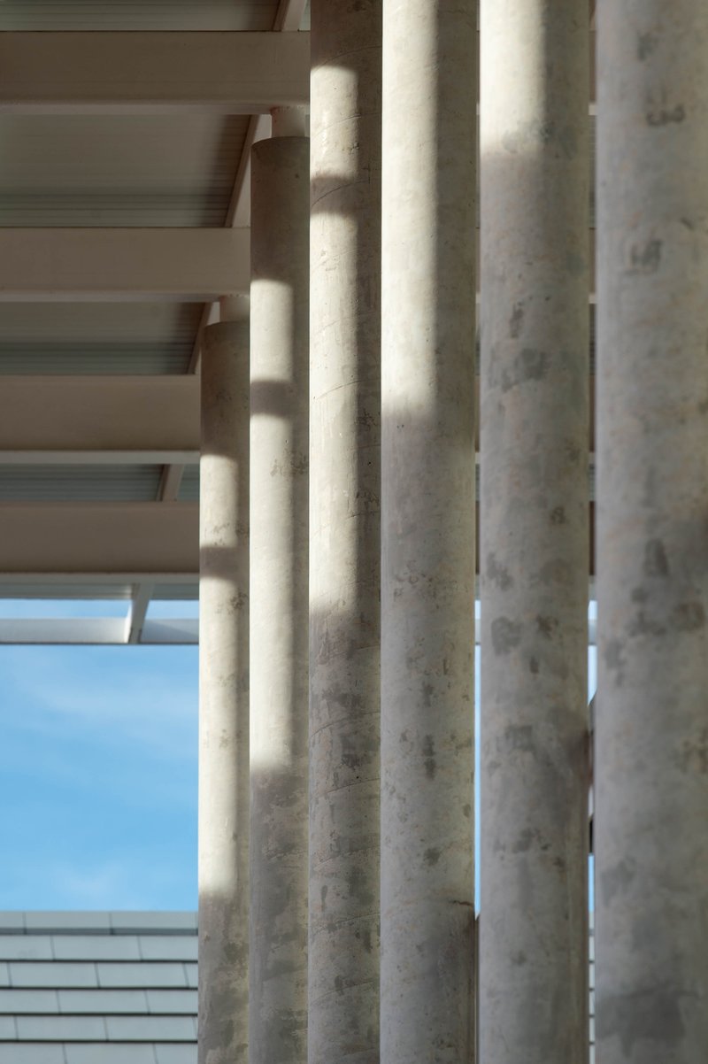 Close-up of cylindrical concrete columns with dappled sunlight filtering through horizontal louvers above