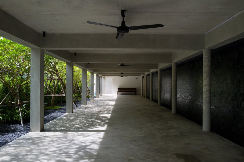 Covered corridor with concrete columns and ceiling fans beside planted bed with lush green foliage
