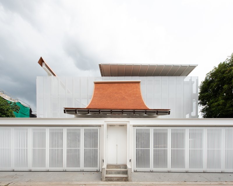 Street view of white vertical slat fence with central entry steps under a curved terracotta roof