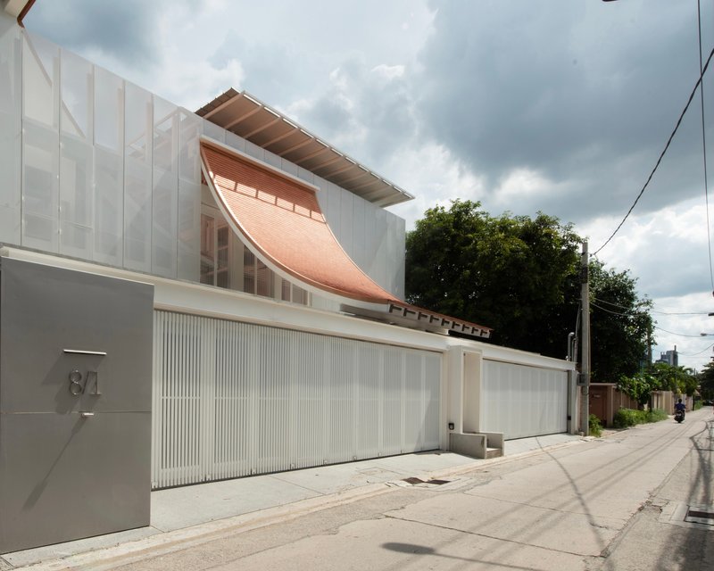 Street view of the white paneled facade with curved clay tile roof element under cloudy skies