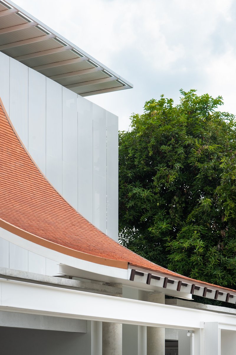 Detail of the terracotta tile roof curving past white vertical paneling with trees beyond