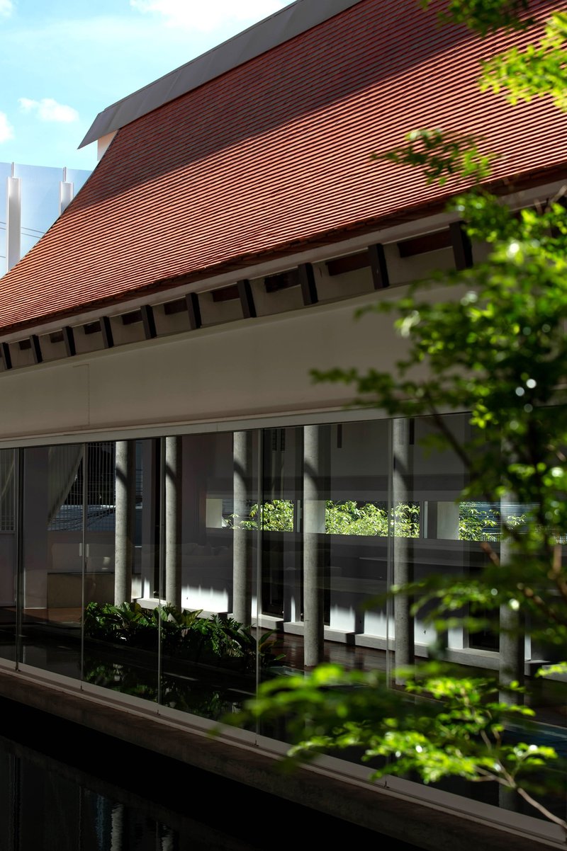 Covered walkway with exposed timber brackets beneath the ribbed terracotta roof framed by greenery