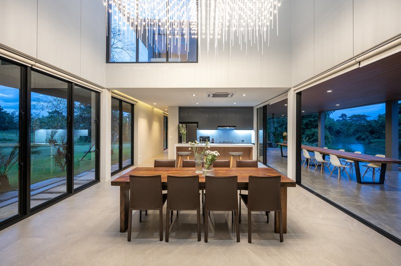 Open-plan dining and kitchen space with sliding glass walls opening to the lawn at twilight