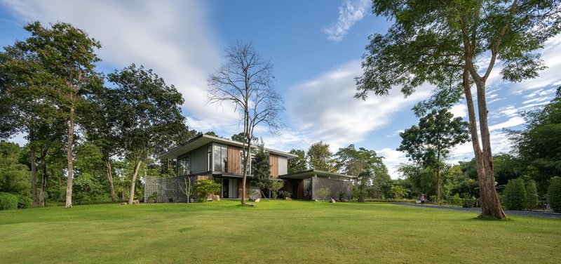 Rear elevation showing stacked volumes of stone and timber siding among tall deciduous trees
