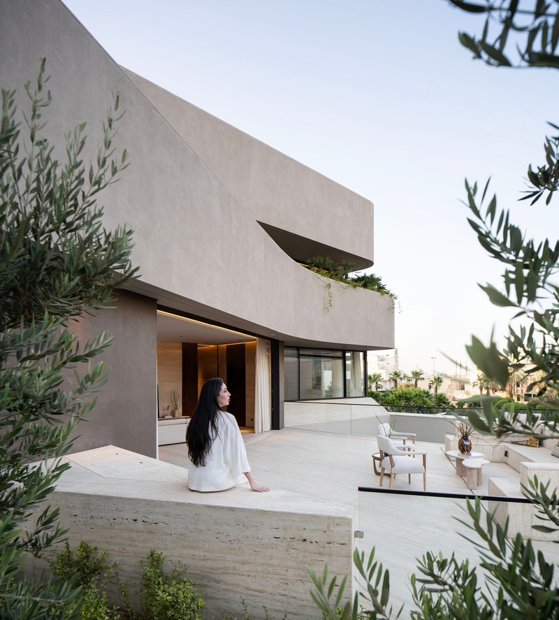 Roof terrace with cantilevered planter and woman in white seated near olive trees at twilight