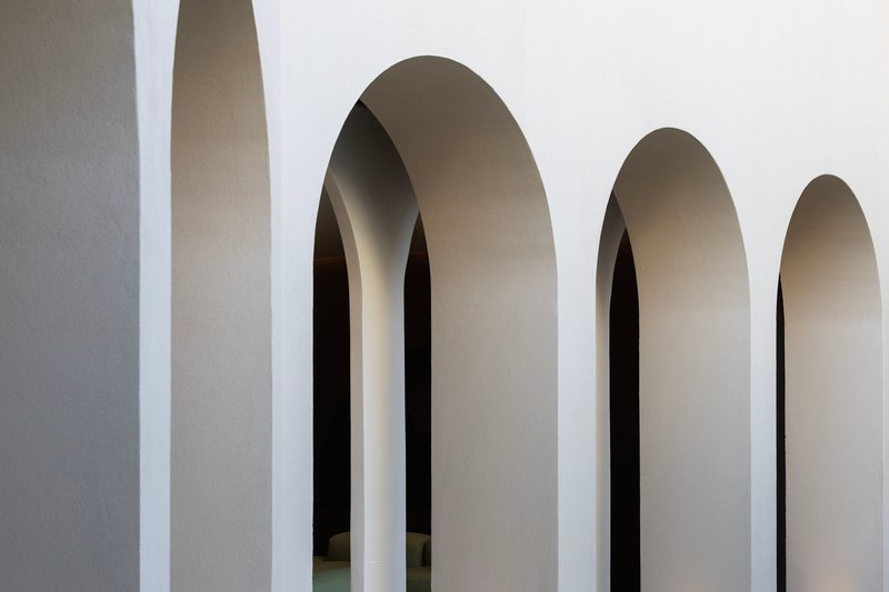 Sequence of tall arched openings with smooth plaster reveals receding into shadow