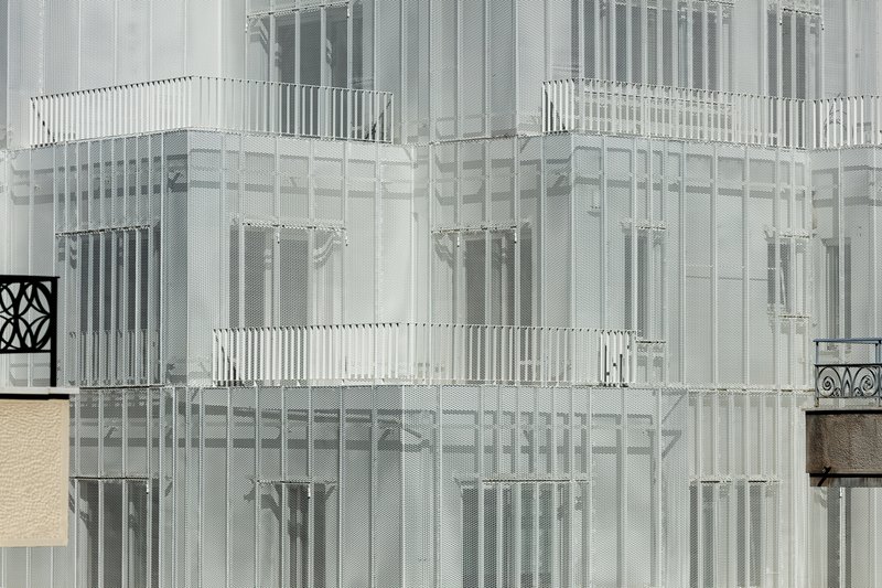 Close-up of the translucent perforated metal panels and vertical louvers wrapping the upper floors