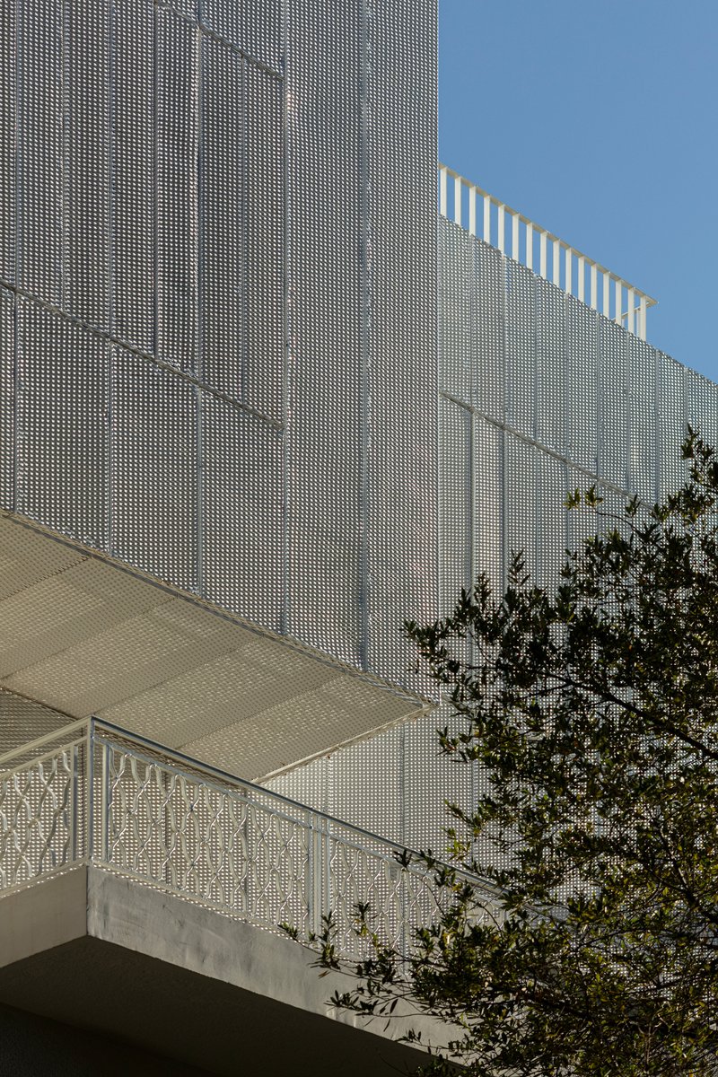 Angled view of the perforated metal screen wall with rooftop pergola slats against a clear sky