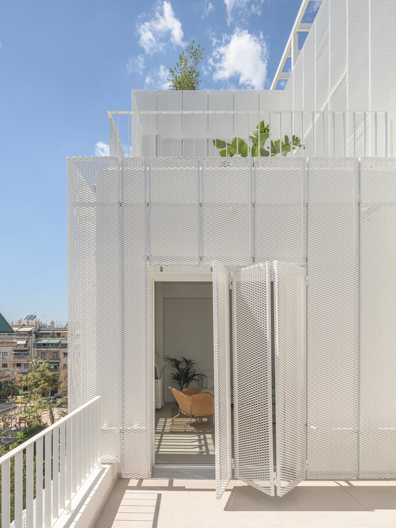 Rooftop terrace with white perforated metal screens, planted bed, and sliding glass door beneath clouds