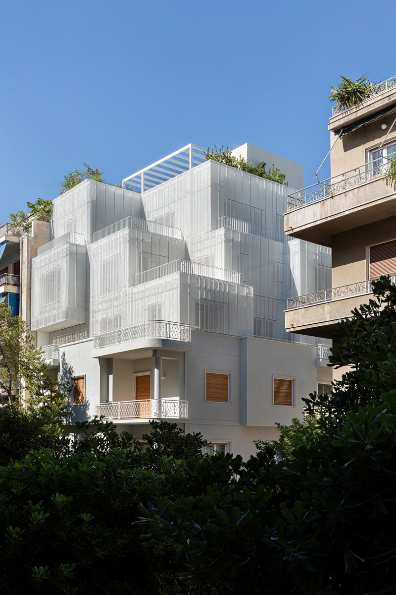 Street view of the layered white metal screen facade with rooftop garden framed by neighboring buildings