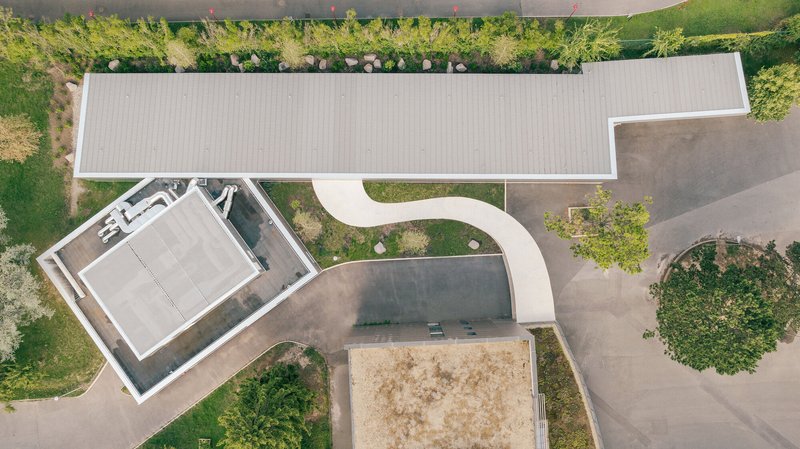 Aerial view of curving concrete canopy connecting linear volumes around planted courtyards and parking areas