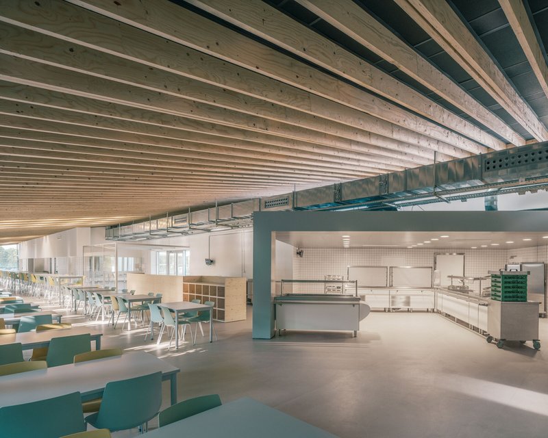 Exposed timber ceiling joists above cafeteria seating area and service counter with mechanical ducting