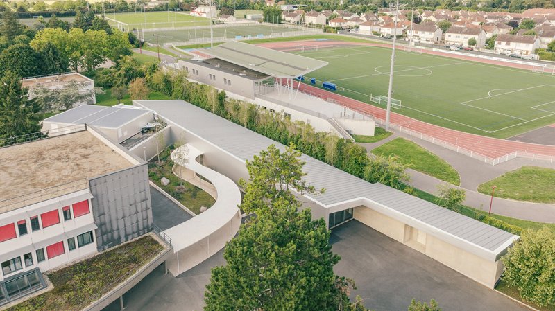 Aerial view of the curved concrete canopy connecting the buildings beside athletic fields