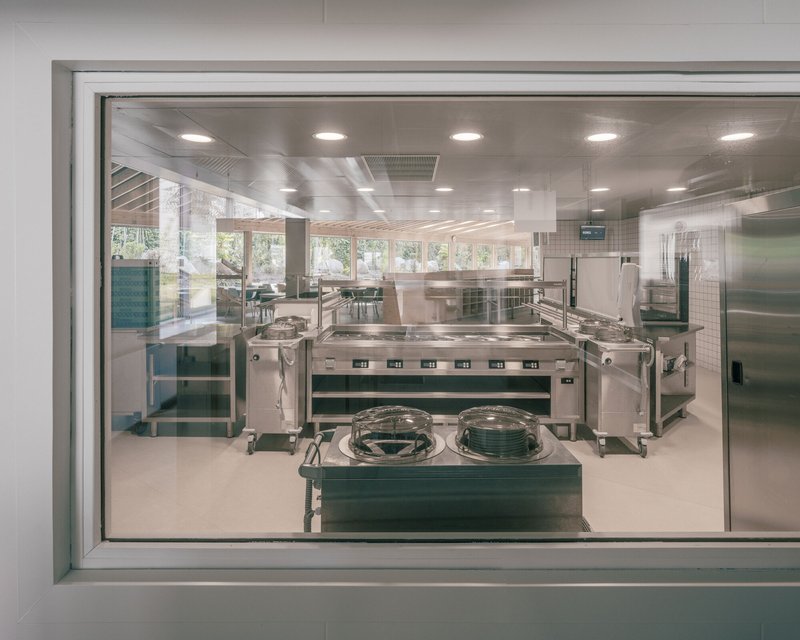View through serving window into the stainless steel commercial kitchen with equipment islands