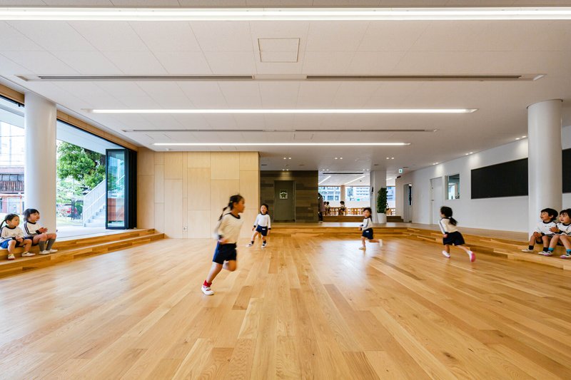 Multi-purpose room with stepped timber seating along one wall and children playing across the floor