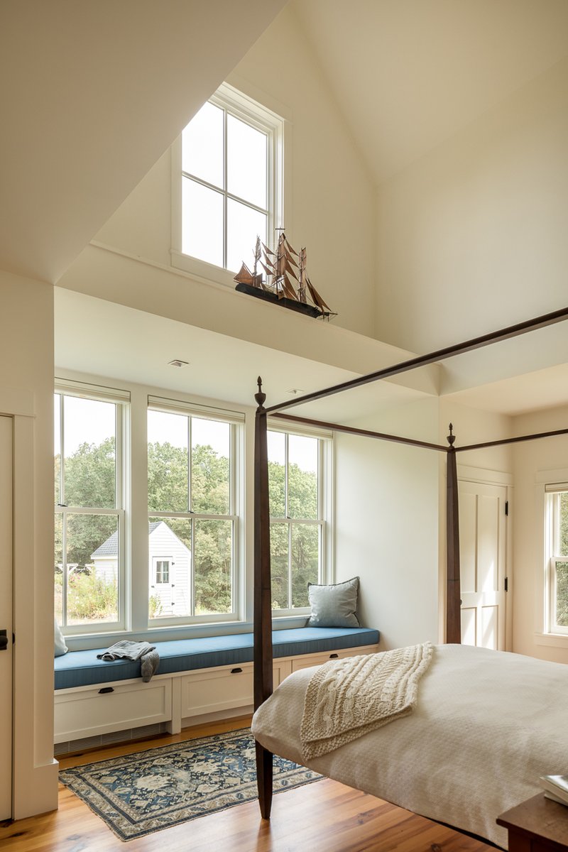Bedroom with built-in window seat beneath tall windows overlooking trees in summer
