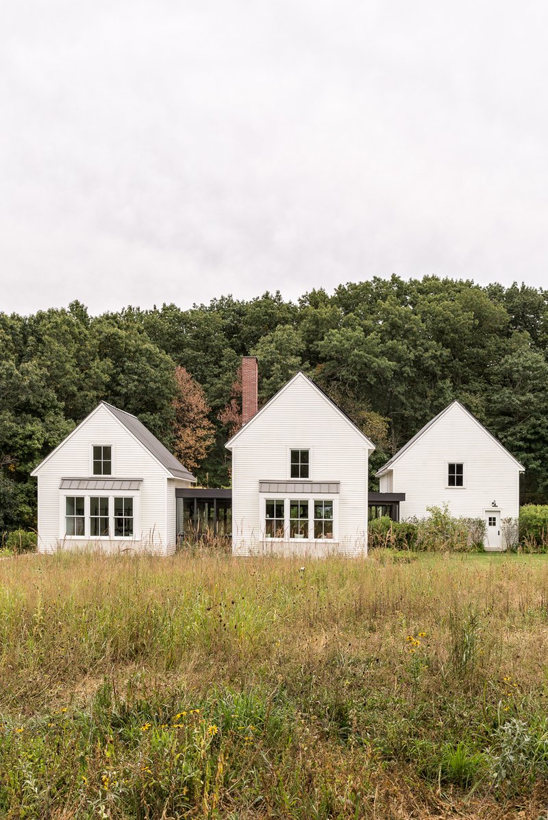 Rear elevation of three connected gabled structures with horizontal siding and brick chimney