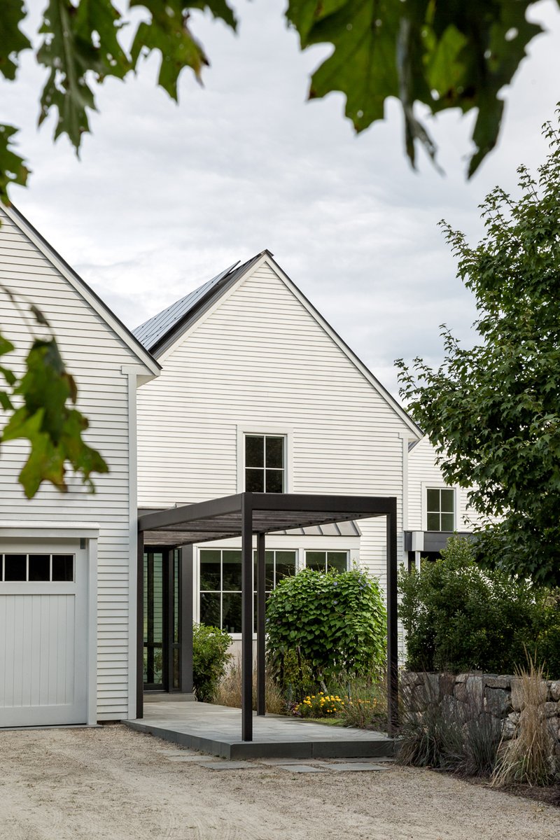 Steel and timber canopy framing the entrance beneath white gabled volumes seen through tree branches