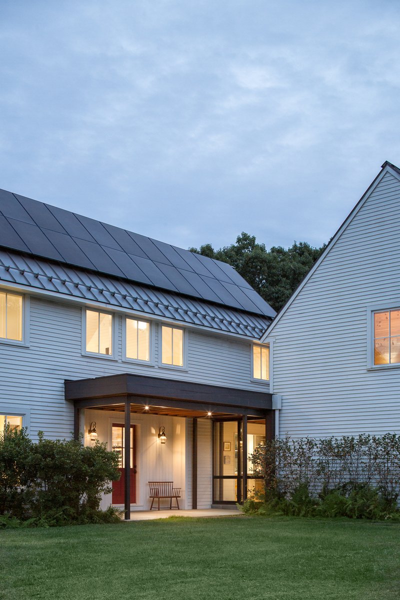 Covered porch with timber posts beneath white siding and solar panels on the gabled roof at dusk