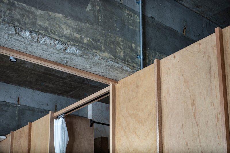 Skylight framed by raw concrete soffit above plywood partitions with warm interior glow