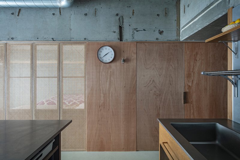 Perforated wood pegboard panels with sliding doors and round clock beneath exposed concrete ceiling