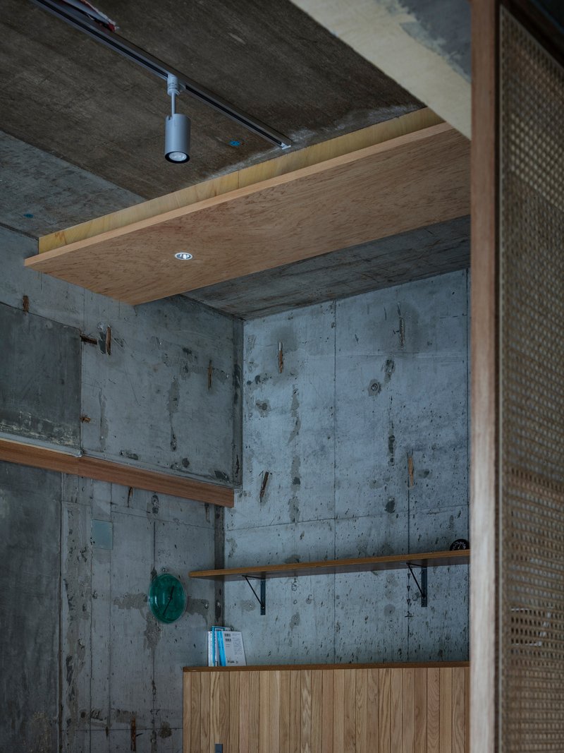 Corner view showing suspended timber ceiling panel and horizontal shelves mounted on exposed concrete