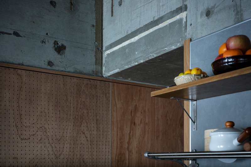 Close-up of perforated wood cabinet edge meeting steel shelves with ceramic containers beneath concrete beam
