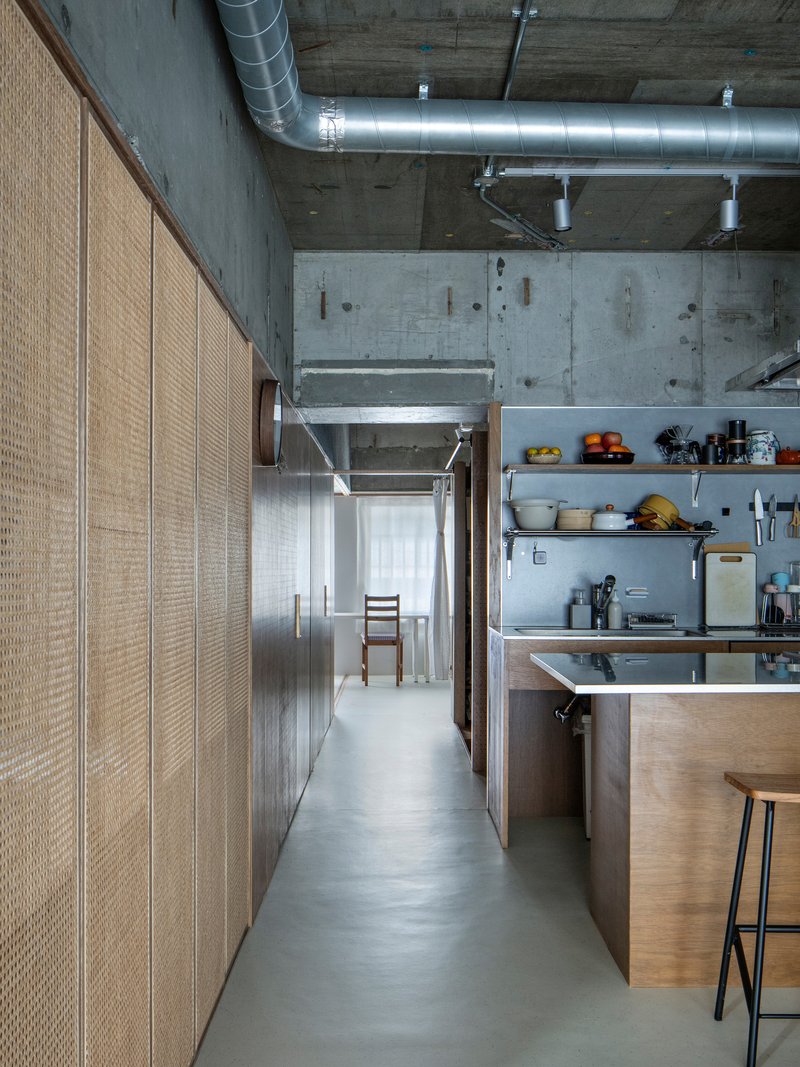 Corridor with woven rattan storage cabinets and open kitchen shelving under exposed concrete and ductwork