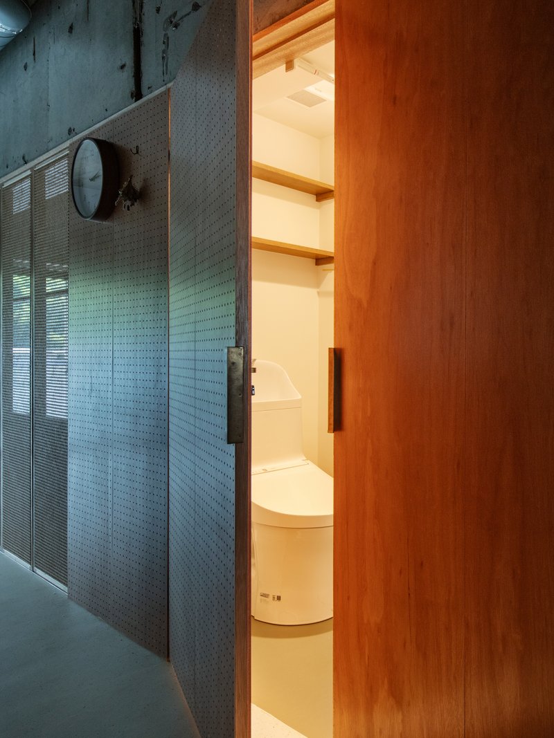 Open sliding door revealing compact bathroom with illuminated shelving and wall-mounted clock outside
