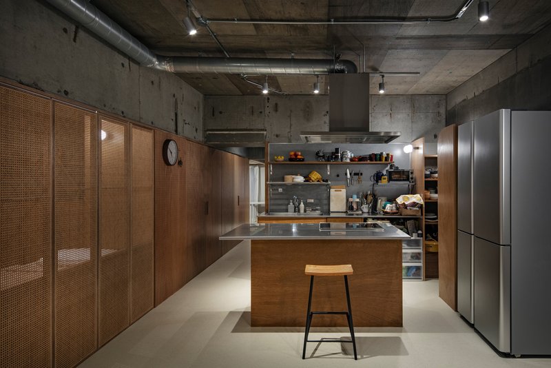 Kitchen island with stainless steel countertop, timber cabinetry and cane sliding panels against raw concrete walls