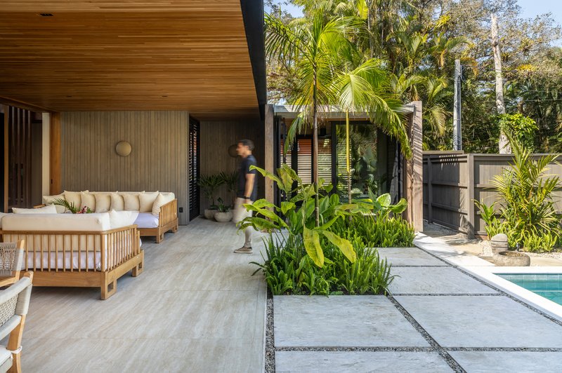 Covered outdoor lounge with timber ceiling and a figure walking past tropical plantings