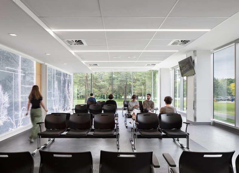Waiting area with rows of black seating and floor-to-ceiling windows overlooking green landscape