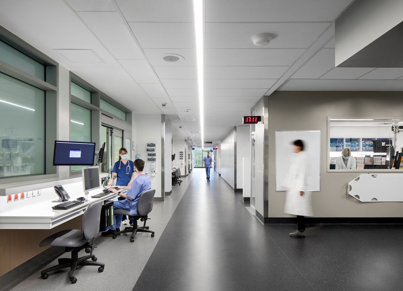 Corridor view with reception desks along one side and medical staff moving through white-walled spaces