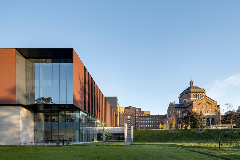 Glass and copper-toned panel facade viewed across a sloping lawn with a domed building in the background