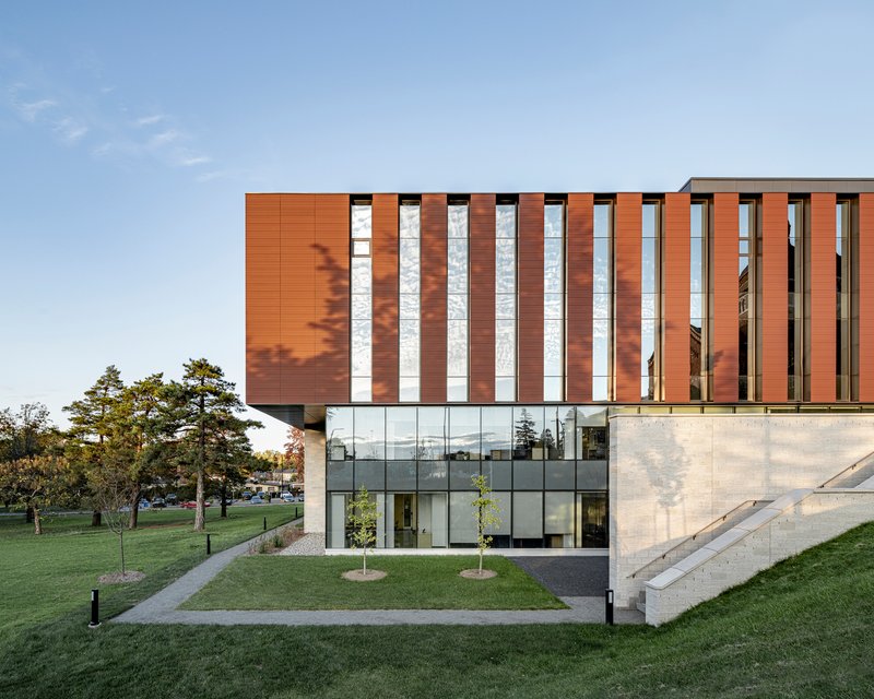 Vertical striped facade with copper and white panels above a glazed concrete base at dusk