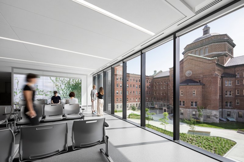Interior classroom with floor-to-ceiling glazing overlooking a landscaped courtyard and adjacent brick building