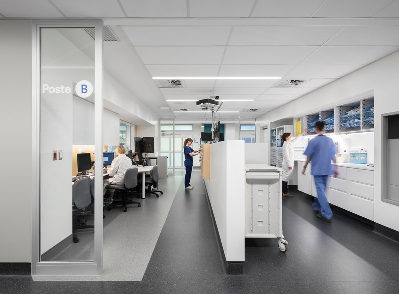 Interior workstation corridor with white casework and medical staff in motion under suspended tile ceilings