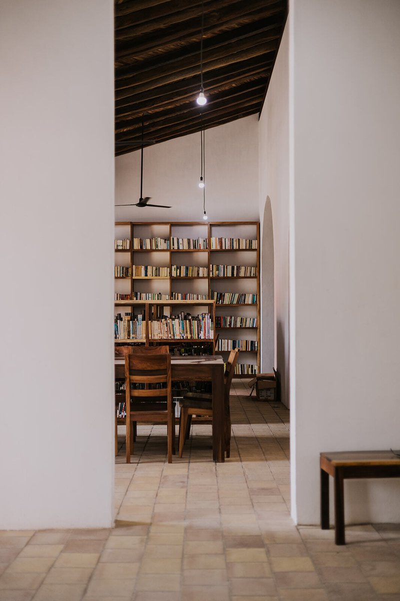 Timber dining table and chairs beside a bookshelf under an exposed rafter ceiling
