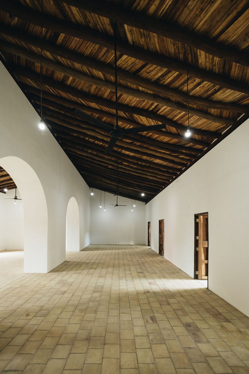 View along the gallery corridor showing layered bamboo roof structure with pendant lighting between white arches