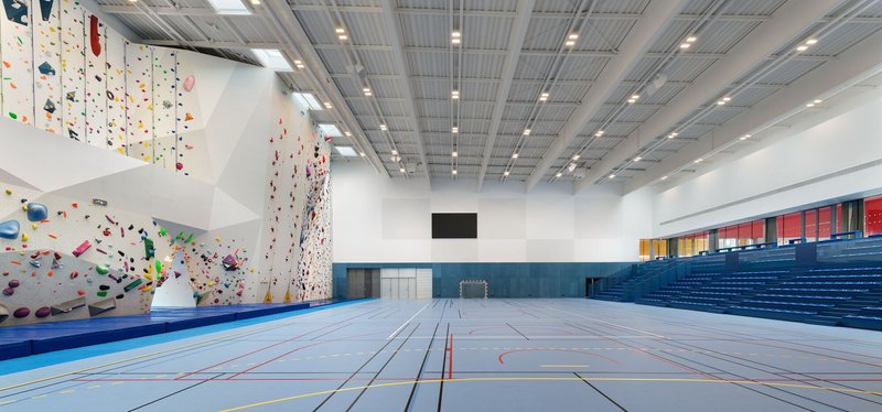 Multi-use sports hall with climbing wall, tiered blue seating, and exposed metal deck ceiling